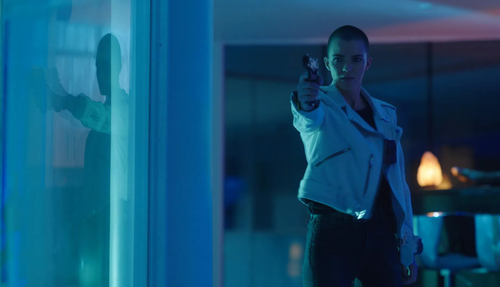 A woman points a pistol at someone in a dark room.